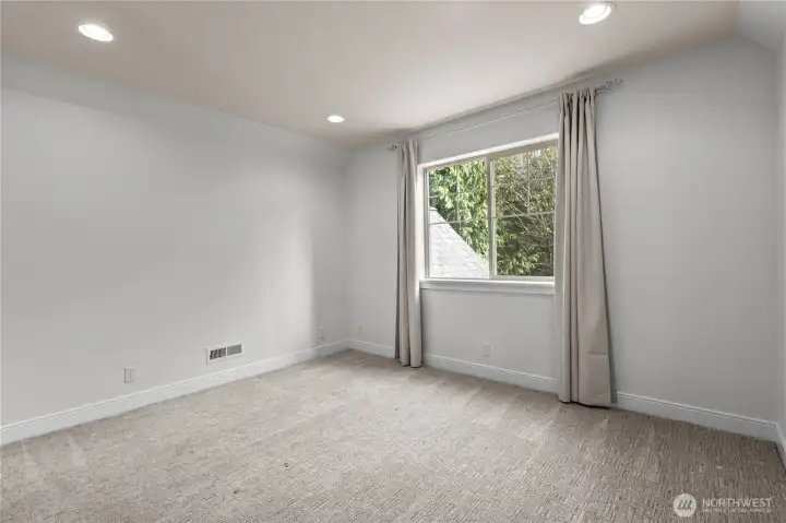 Second bedroom with carpet, neutral finishes, and window overlooking surrounding trees.