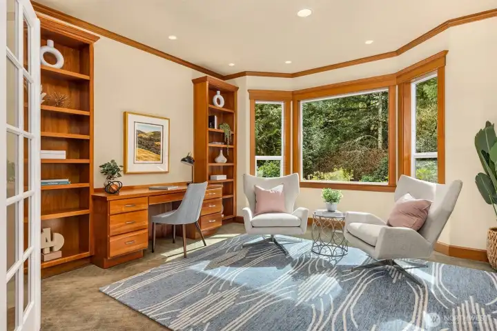 Den/home office has French doors, built-in desk and bookshelves, and large windows overlooking gardens.