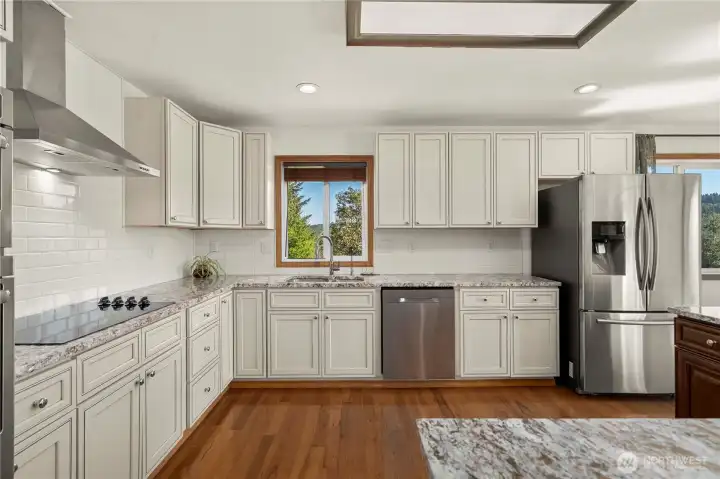 Bright, spacious kitchen with abundant cabinetry, granite counters, stainless appliances, and a window over the sink that brings in natural light and a peek of the view.