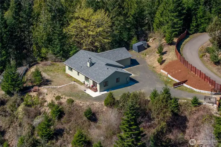 Aerial view shows the home’s private setting with a wide driveway, attached garage, and gated entrance—nestled among evergreens on 3.8 acres for true peace and seclusion.