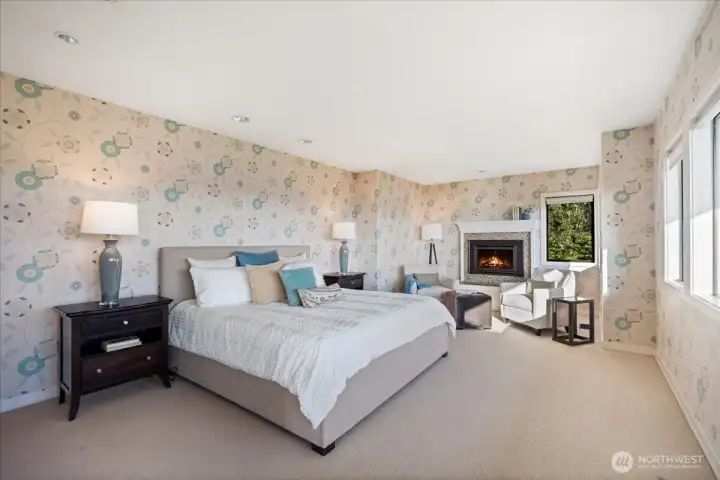 Spacious primary bedroom with custom wallpaper and a cozy fireplace insert.