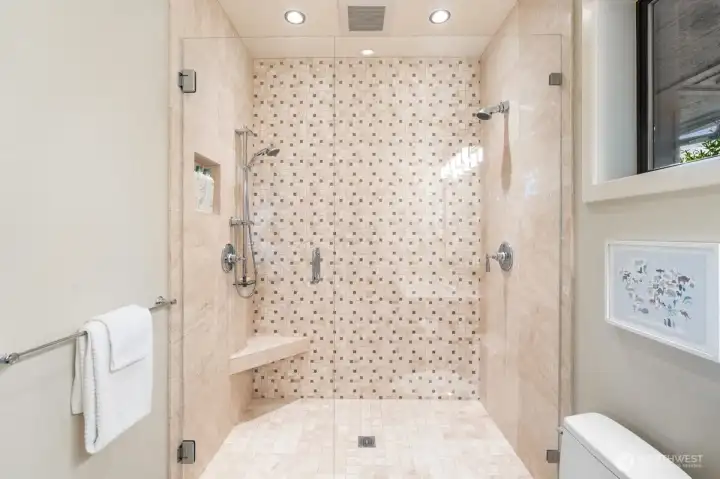 The extra-large shower features floor-to-ceiling tile, dual shower heads, and a built-in bench, offering comfort and functionality for a wide range of ages and needs.