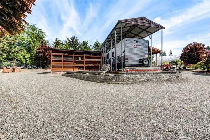 Opposite the shop, a covered RV structure with adjacent storage bays and expansive gravel parking provides exceptional space for recreational vehicles, trailers, equipment, and outdoor storage.
