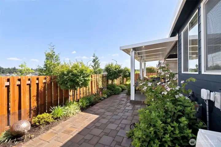 Privacy is one of the unexpected luxuries of this backyard. Rather than staring directly into neighboring homes, this property backs to a small greenbelt area and the street beyond, creating a much more open and comfortable feel. The beautifully designed paver patio and pathways weave through thoughtfully planned landscaping that delivers color, texture and interest throughout the seasons. Some plantings provide cheerful blooms while others offer evergreen structure and year-round beauty. A handsome cedar fence frames the space, creating a backyard that feels polished, private and wonderfully low maintenance. It's the perfect setting for morning coffee, evening conversations or simply enjoying a little peace and quiet after a busy day at the clubhouse.