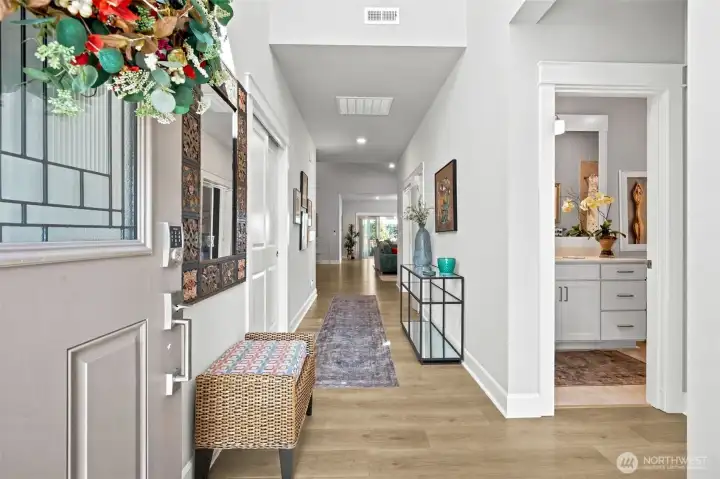 The moment you step inside, this home makes a wonderful first impression. A handsome front door with decorative leaded-glass detailing welcomes guests into a bright foyer, while the keyless entry system adds everyday convenience and peace of mind. From this vantage point, you can immediately appreciate the thoughtful layout, with the front guest wing located just off to the right, offering easy access to both the bedroom and full bathroom. A spacious coat closet helps keep everyday essentials neatly tucked away, while the hallway beyond gently guides you toward the main living spaces.