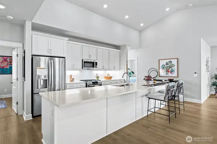 Let's be honest: everyone is ending up around this island. It's enormous. With room for approximately six stools, this oversized quartz centerpiece transforms the kitchen into the ultimate gathering space where meals, conversations, celebrations and morning coffee routines all naturally happen. The surrounding white shaker cabinetry and stainless appliances provide timeless style, while the French-door refrigerator with water and ice service keeps refreshments within easy reach. Under-cabinet lighting illuminates prep space beautifully, and recessed lighting scattered throughout the vaulted ceiling ensures the room feels bright and inviting at any hour.