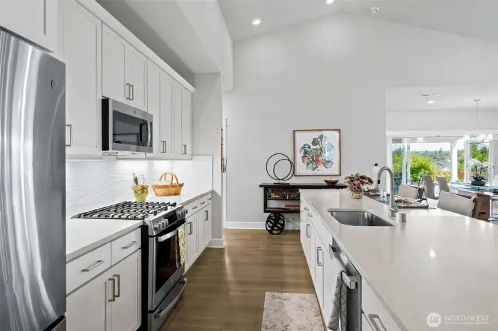 The kitchen’s showpiece island is generously sized for casual dining, charcuterie spreads, holiday baking marathons and all the conversations that inevitably happen around a great kitchen. Quartz countertops, a large undermount sink, pull-down faucet and stainless steel gas range combine beauty and practicality, while the sleek white shaker cabinetry keeps the entire space feeling fresh and current. A textured white subway tile backsplash adds subtle dimension, and the vaulted ceiling overhead gives the room an even larger, brighter feel.