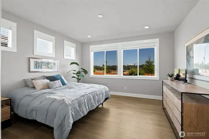 This spacious primary suite was thoughtfully designed to maximize both privacy and flexibility. Three clerestory-style windows positioned high on one wall allow for easier furniture placement while still bringing in abundant natural light, and each is equipped with adjustable blinds so you can customize the ambiance to your liking. Then your eye is immediately drawn to the true showstopper, a pair of large picture windows framing an unobstructed view of Mount Rainier. Around here, locals have a saying: "The mountain is out." In this room, you'll know exactly what they mean. Imagine waking up each morning to one of the Pacific Northwest's most iconic views right from the comfort of your bed.