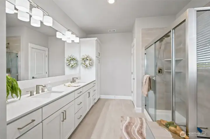 Now this is a primary bath that understands storage. The extra-long dual-sink vanity provides enough room for two people to comfortably get ready at the same time, while the tall spa-style linen cabinet keeps towels, toiletries and extras neatly tucked away. A dedicated water closet adds privacy, allowing the space to function beautifully when when schedules overlap. The shower is large, elegant and finished with a low-threshold entry an dual showerheads that bring a touch of spa-inspired luxury to everyday life.