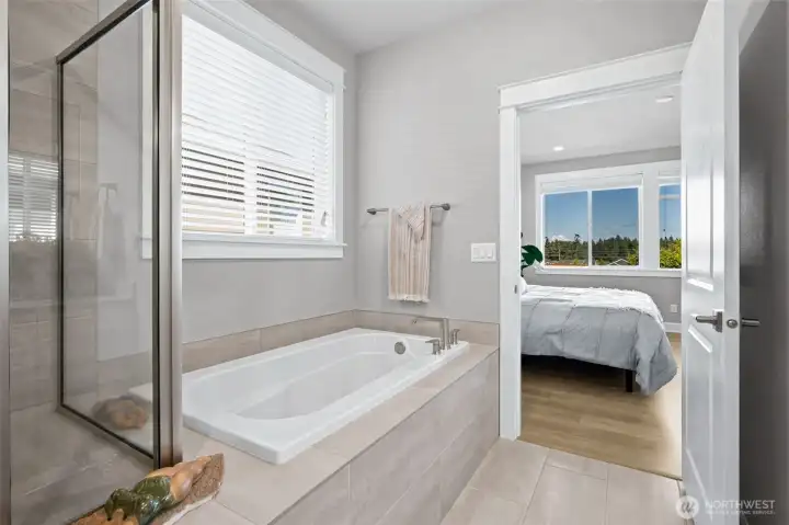 Go ahead and pour the bubble bath. This gorgeous soaking tub creates the spa moment every primary suite deserves, tucked beneath a large window that brings in beautiful natural light while still allowing privacy when desired thanks to adjustable blinds. It's easy to imagine ending the day here with a good book, a glass of wine and absolutely no plans. Beyond the tub, the thoughtful layout continues to impress with generous space and elegant finishes throughout the primary bath. Then, when you step back into the bedroom, Mount Rainier is waiting to steal the spotlight all over again.