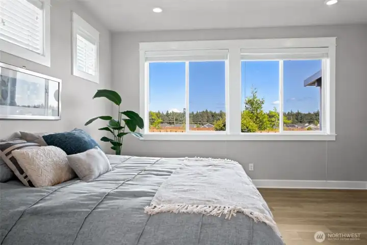 Wake up, roll over and check whether "the mountain is out" without ever leaving your bed. This closer view of the primary suite highlights one of the home's most special features: that postcard-worthy Mount Rainier view peeking above the treetops. The soft warm-gray walls create a calming retreat at the end of the day, while crisp white ceilings help reflect natural light throughout the room and keep the space feeling bright and airy. Large windows frame the scenery beautifully, creating a peaceful connection to the outdoors while still maintaining the privacy that makes this primary suite feel like a true escape from the rest of the world.