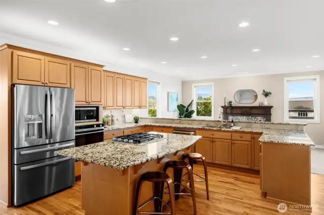 Gourmet kitchen with granite slab counters, on point tile backsplash with deco accent, gas cooktop island, stainless-steel appliances, walk in pantry and built in work desk.