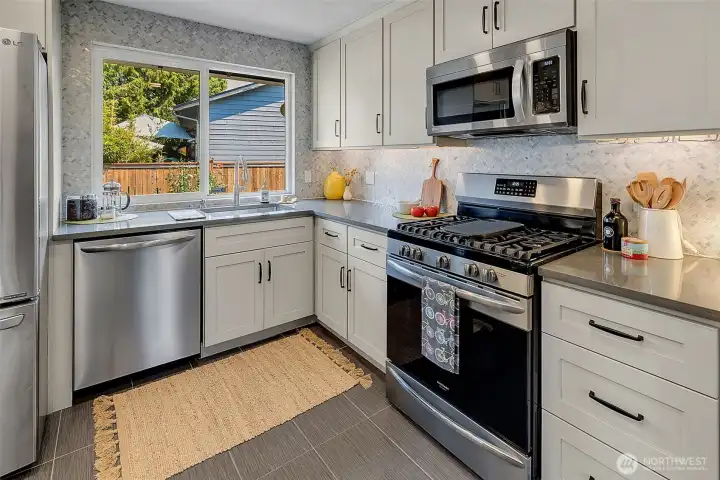 Updated kitchen with ceramic tile floors, quartz countertops, marble tile accent backsplash, shaker cabinets, and a full suite of stainless steel appliances, including a built-in microwave and a 5-burner gas range.
