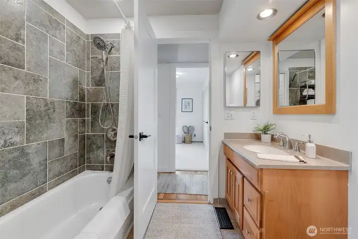 Full bath with tiled surround opens to both the hallway and the primary bedroom on the other side.