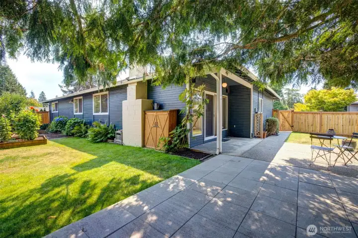 Fully fenced backyard with raised garden beds, a level paver patio, and lawn. Mature landscaping with established plants and trees.