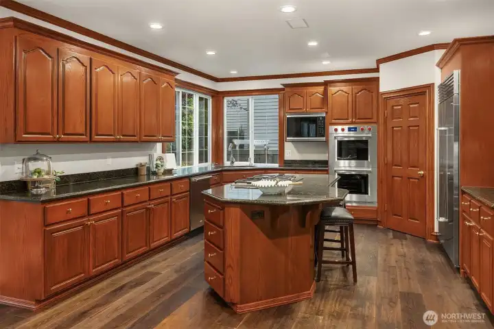 The chef’s kitchen features premium, professional-grade appliances, including a built-in Sub-Zero refrigerator, new Wolf double convection ovens, Wolf convection microwave, and a Cove (Wolf) dishwasher, all complemented by slab granite counters and a spacious center island.