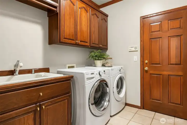 Main level laundry room connects to the 3-car side-by-side garage and features a side-by-side washer dryer, plenty of storage, tile flooring and a utility sink. All appliances will stay with the home.