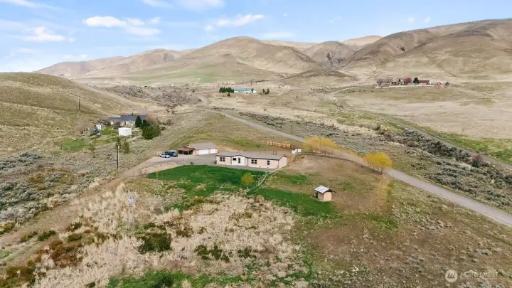 Centered aerial capturing the home, shop, and surrounding land, emphasizing usable space and the peaceful rural setting.