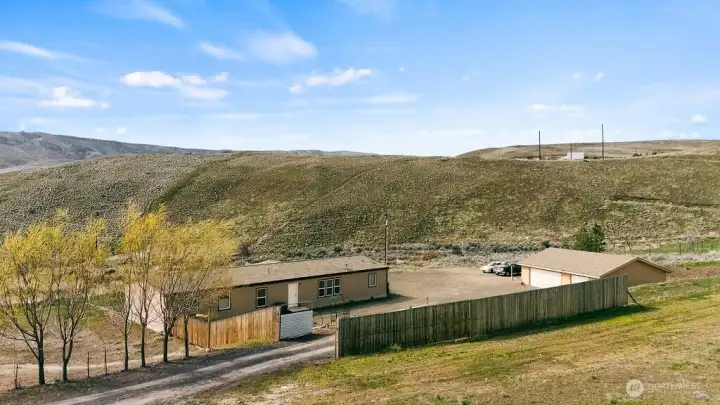 Aerial capturing the gated entrance, driveway, home, and shop—highlighting privacy, security, and the full property footprint.