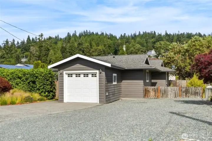 Front exterior with the 1-car garage and a wide gravel driveway, framed by ornamental grasses and Japanese maple, fencing and hedge. Front exterior with the 1-car garage and a wide gravel driveway, framed by ornamental grasses and Japanese maple, fencing and hedge.