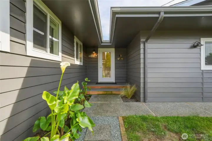 Covered entry with a concrete walkway, calla lily plantings, and nautical-themed wall accents. Covered entry with a concrete walkway, calla lily plantings, and nautical-themed wall accents.