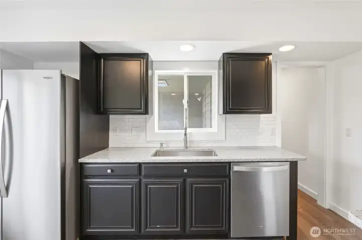 Sink centered beneath a window, flanked by quartz counters and a stainless dishwasher. Sink centered beneath a window, flanked by quartz counters and a stainless dishwasher.