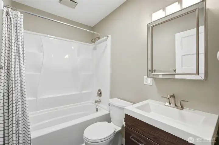 Full bathroom with a tub/shower combo, dark wood vanity, and a framed mirror above the sink. Full bathroom with a tub/shower combo, dark wood vanity, and a framed mirror above the sink.