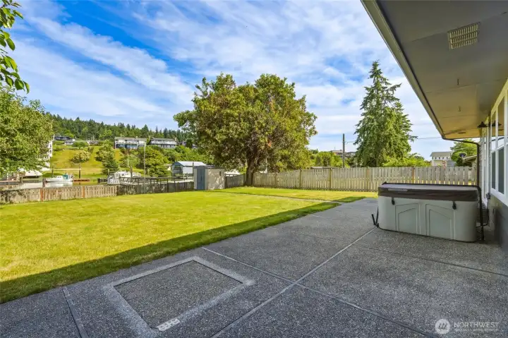 Backyard patio with a covered hot tub and a glimpse of the canal and boat moorage beyond the fence. Backyard patio with a covered hot tub and a glimpse of the canal and boat moorage beyond the fence.