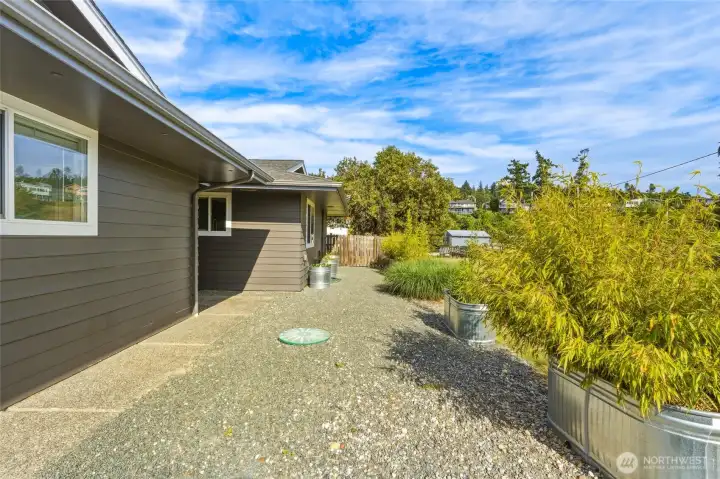 Gravel side yard with septic access cover and container gardens of bamboo and ornamental grasses. Gravel side yard with septic access cover and container gardens of bamboo and ornamental grasses.