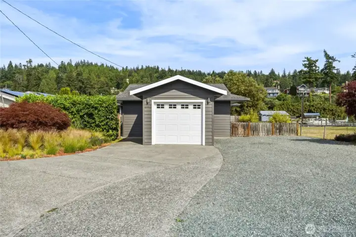 Garage, driveway and gravel parking area with canal moorage visible beyond the side fence. Garage, driveway and gravel parking area with canal moorage visible beyond the side fence.