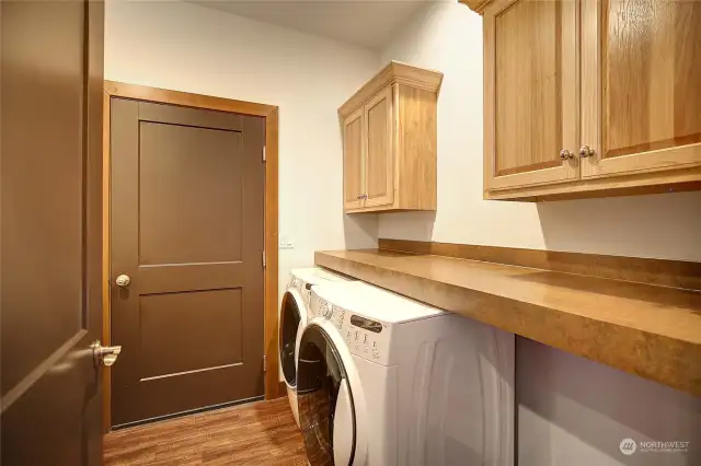 Laundry room leading to the garage with countertops for folding clothes and cabinets for storage