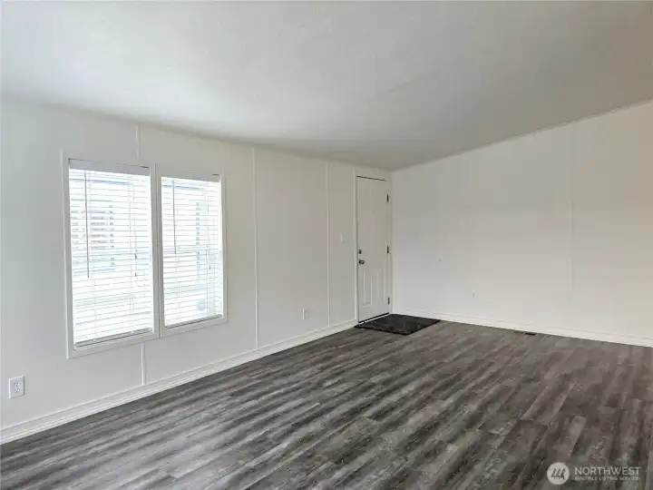 Spacious and inviting living room filled with natural light from windows on two walls, creating a bright and airy feel. Blinds are already in place for privacy and light control, making this space both comfortable and move-in ready.