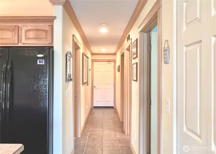 Hallway Leading to the Garage, with the   Primary Bedroom and En-Suite to the Left.   The Three Doors on the Right Lead to Two   Additional Bedrooms and a Full Bathroom.