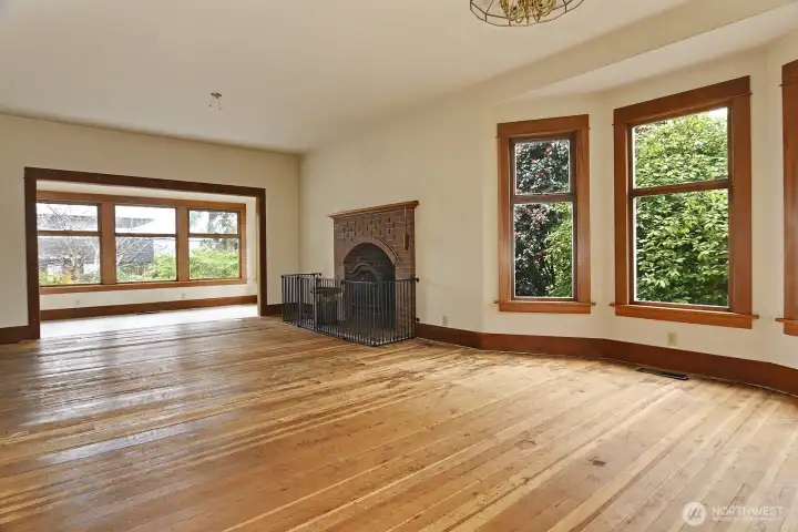 An angle showing the gracious size of the living room, with beautiful mature flowering bushes outside.