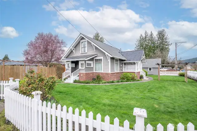 Corner lot with white picket fencing and mature landscape with blossoming bulbs and perennials