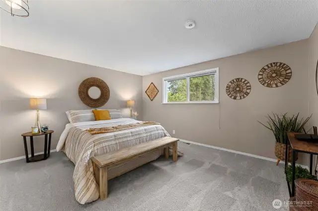 Large primary bedroom with new carpet overlooks the backyard