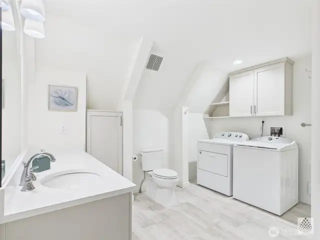 This updated main-floor second bathroom doubles as a laundry space and features a custom cabinet with silestone countertops and durable and elegant LVP flooring.