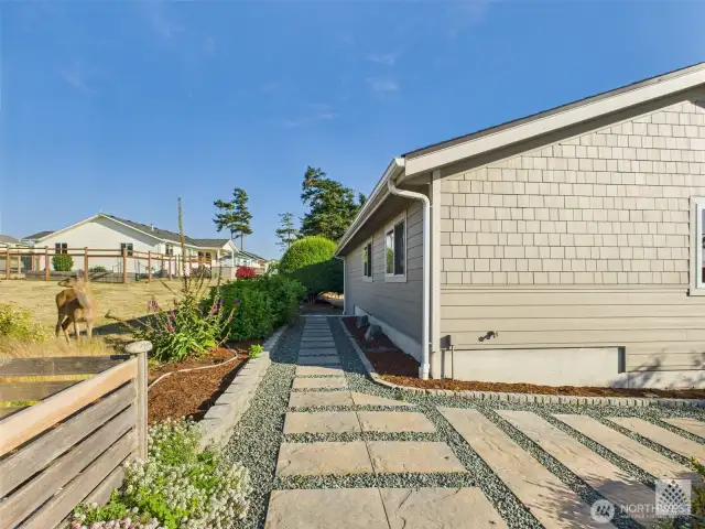 A beautifully crafted stone path wraps around the side of the home and garden, offering convenient access for tending plants and maintaining the outdoor space.