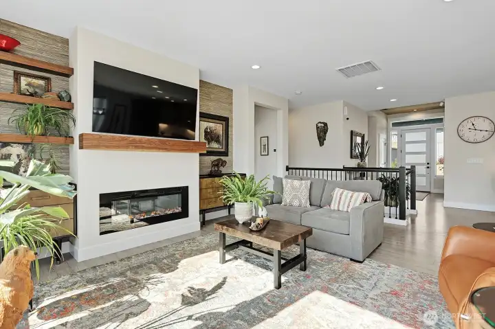 Great room with fireplace and television facing back toward the front door of the home.