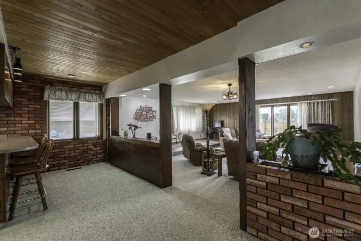 Open-concept living area with wood ceilings, brick accents, and seamless connection to the kitchen and family room.