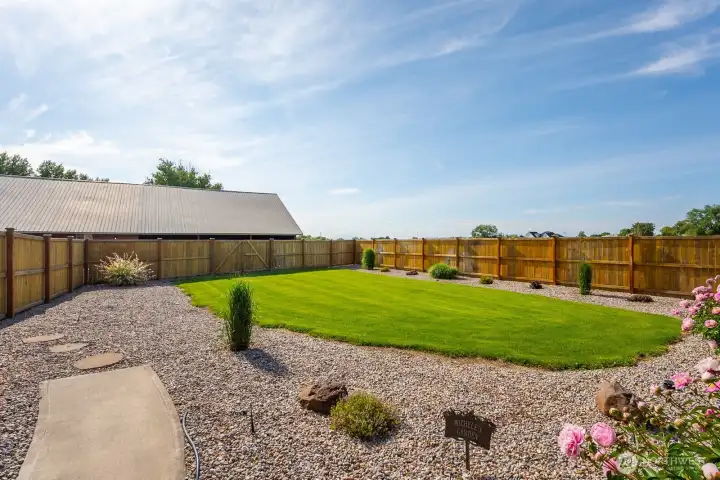 Low-maintenance fenced yard with lush lawn, decorative rock landscaping, and open outdoor space.