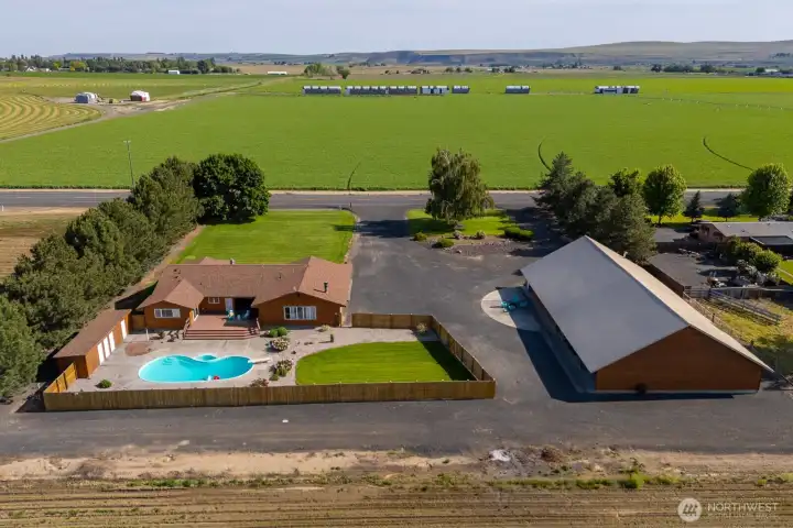 Aerial perspective showcases the home, expansive shop, pool area, and surrounding agricultural views.