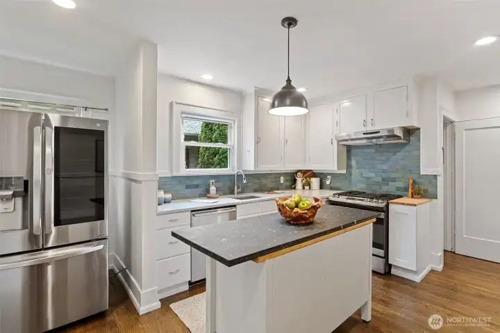 The generous eat-in kitchen offers excellent workspace and storage, highlighted by newer quartz countertops, a stainless undermount sink, white cabinetry, a movable granite-topped island, and a striking blue-green ceramic subway tile backsplash.