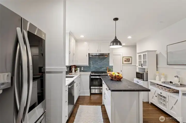 The renovated kitchen shines with updated flooring, quartz countertops, fresh paint, a newer stove, and additional cabinetry that enhances both storage and functionality.