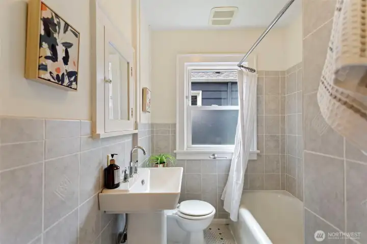 Main floor Full bathroom featuring classic hex tile flooring, a tiled tub and wall surround, and an original built-in mirrored vanity paired with a pedestal sink, blending timeless character with everyday functionality.