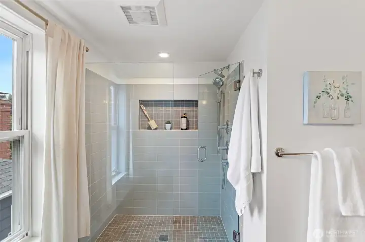 Generous walk-in shower with a tempered glass door, subway tile surround, large built-in niche, and dual rain and handheld showerheads, combining style, convenience, and comfort.
