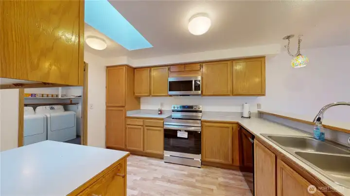 Spacious kitchen with ample cabinetry, counter space, and laminate flooring. Stainless steel appliances including a range and microwave, a double sink, and a skylight that fills the space with natural light.