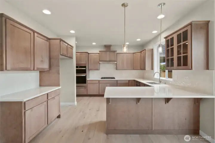Sleek and modern kitchen with quartz counters and full tile backsplash. Pendant lights hang above eating bar are perfect for casual meals or entertaining.