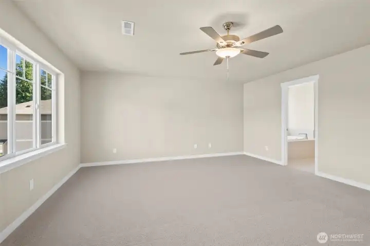 Spacious primary bedroom with carpet flooring creating a soft and calming atmosphere. A ceiling fan with an integrated light fixture is mounted at the center of the ceiling, providing both illumination and airflow.