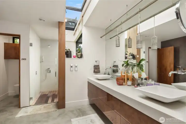 Luxurious primary bath features a floating vanity with vessel sinks and wall mount fixtures. Large, linear skylight illuminates the space with natural light. Dual shower with multiple heads and programmable temperature controls.